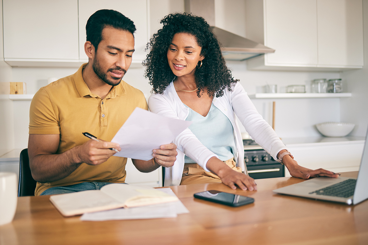 couple seated at kitchen table doing calculations on laptop
